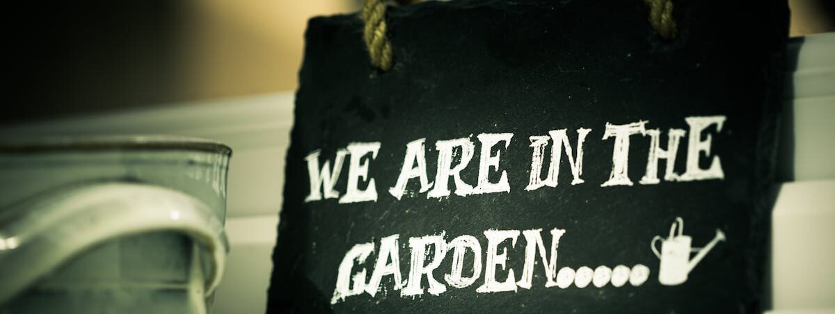 Close-up of a rustic slate sign reading "We Are In The Garden."